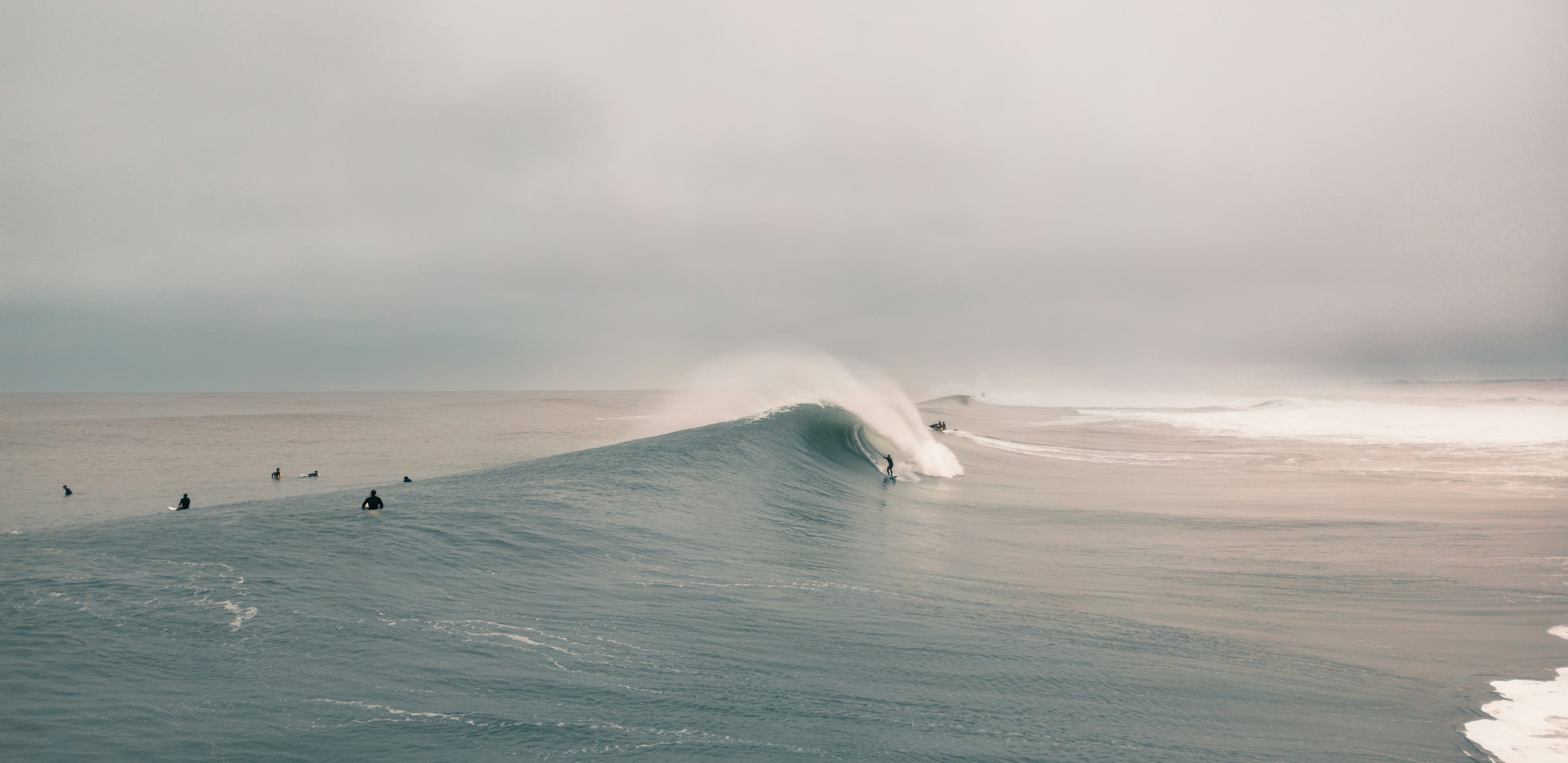 Surfer riding an ocean wave while another person watches from the rocks